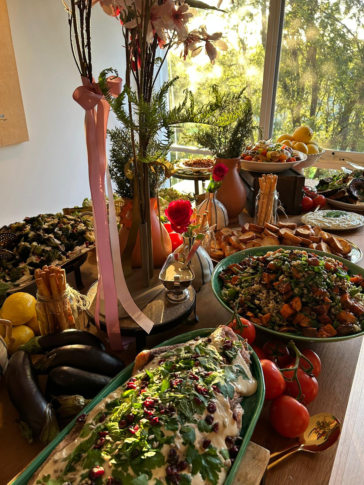 A styled catering table at golden hour, platters, roses and tomatoes